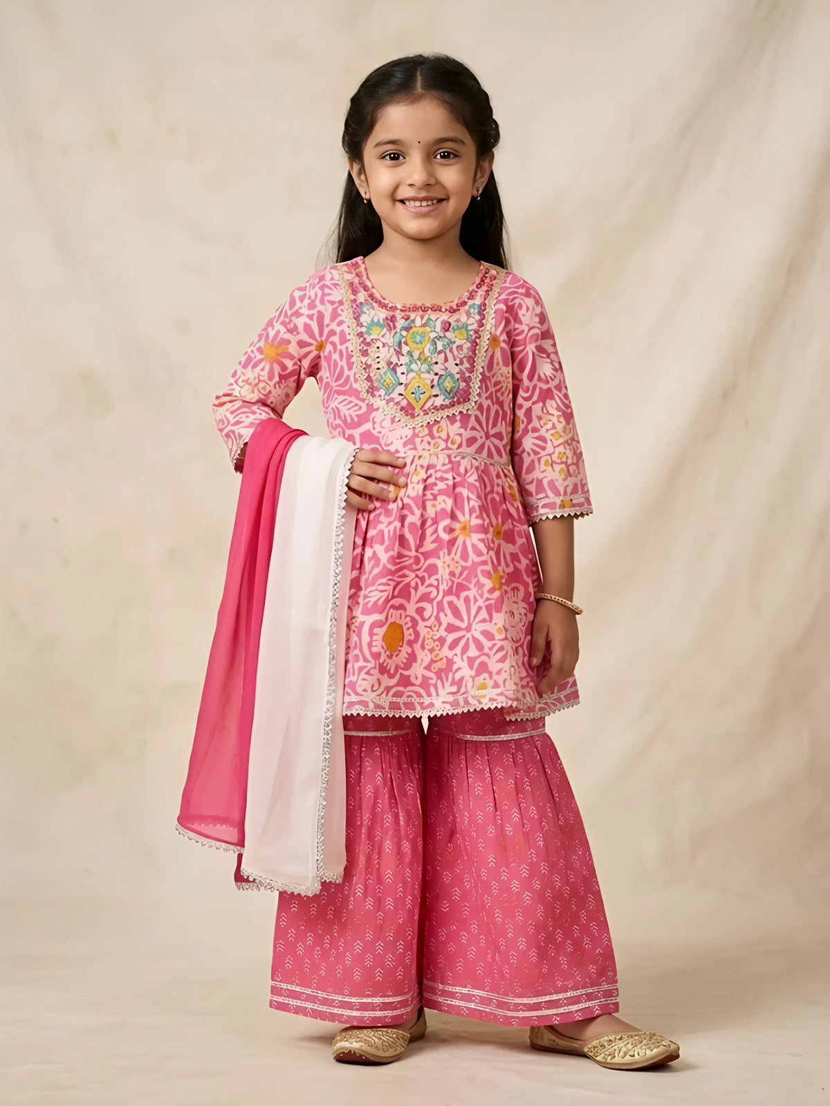 Young girl wearing a pink floral printed short kurta and flared sharara set with dual-tone white and pink dupatta.