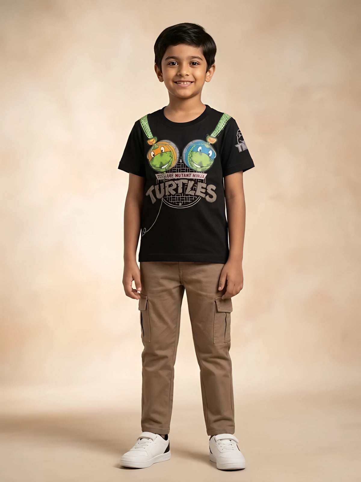 Young boy wearing a black short-sleeve graphic t-shirt featuring Ninja Turtles prints paired with brown cargo pants.