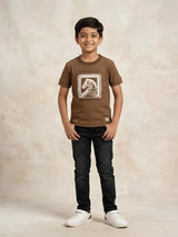 Young boy wearing a brown short-sleeve graphic t-shirt with dark jeans