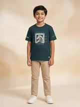 Young boy wearing a dark green short-sleeve graphic t-shirt with beige trousers