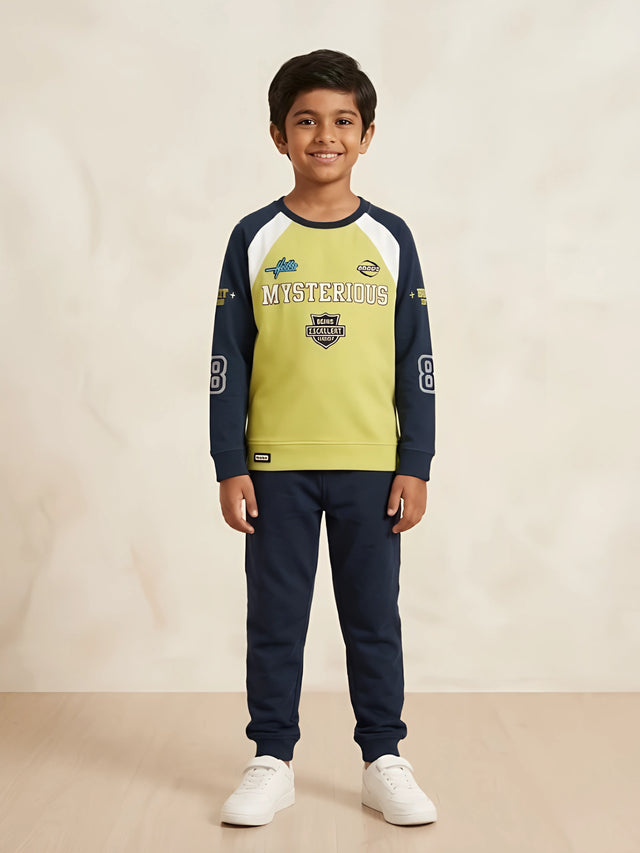 Young boy wearing a green and navy blue full sleeve graphic t-shirt with navy joggers and white sneakers