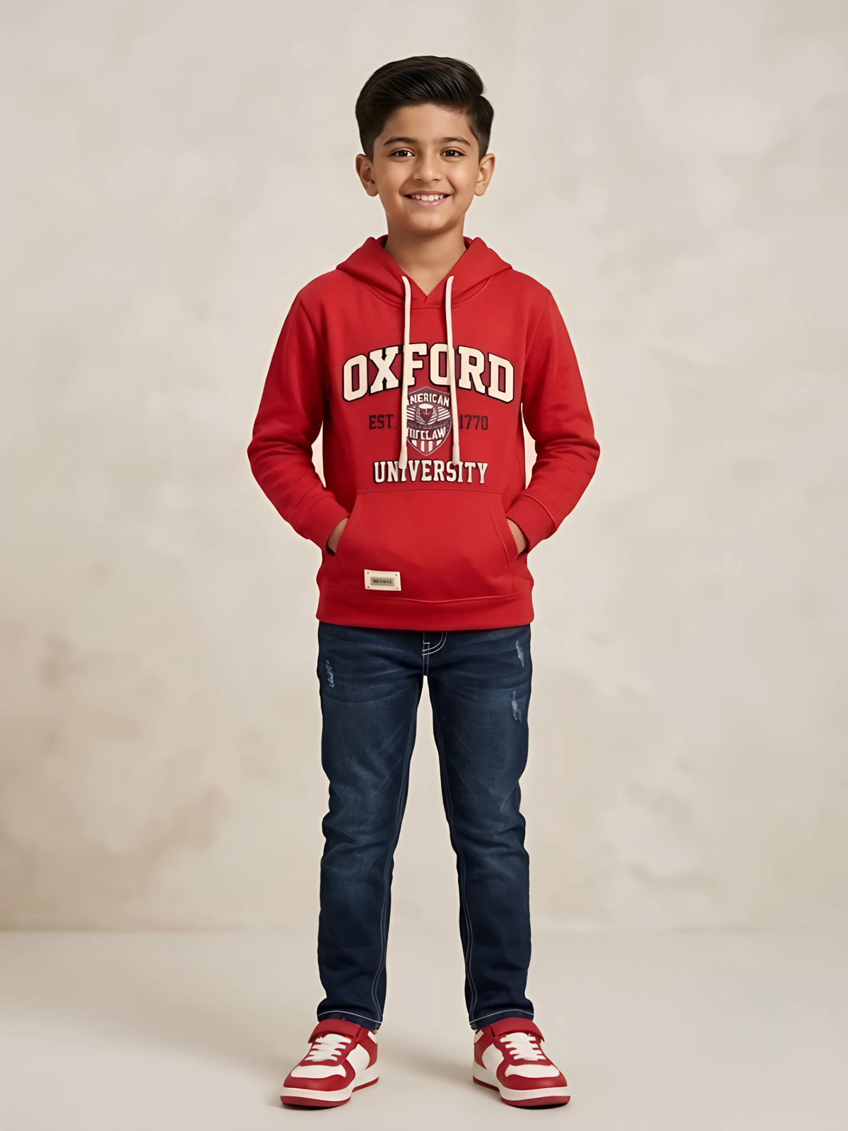 Young boy wearing a red hooded casual t-shirt with Oxford graphic print, white drawstrings, and a front kangaroo pocket paired with dark blue jeans