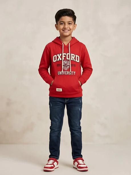 Young boy wearing a red hooded casual t-shirt with Oxford graphic print, white drawstrings, and a front kangaroo pocket paired with dark blue jeans