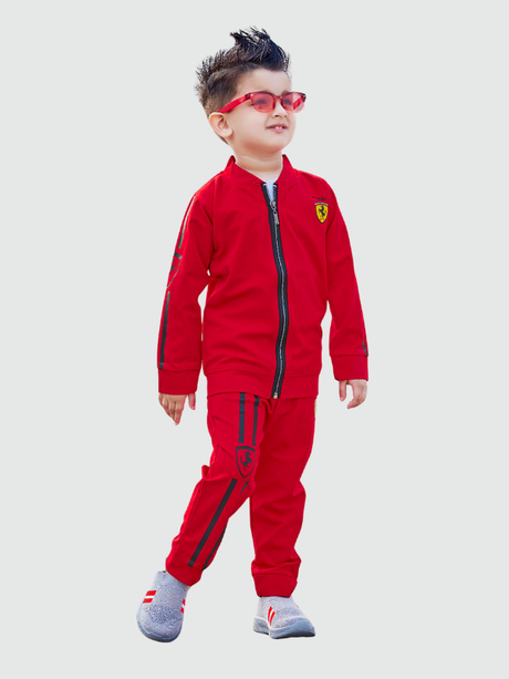 Young boy standing confidently in a full vibrant red tracksuit set, including a zip-up jacket and matching joggers with dark racing stripes. He is wearing sunglasses and gray sneakers.