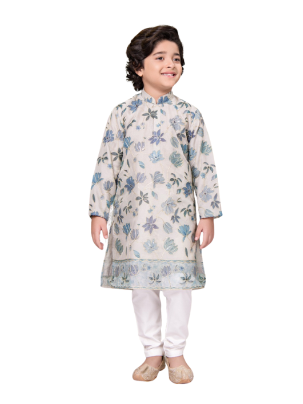 Full-length image of a young boy wearing a cream/off-white traditional kurta with all-over blue floral embroidery and a matching border, paired with white churidar pajamas and gold ethnic shoes.