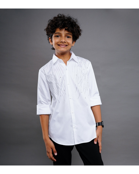 Young boy smiling and wearing a white long-sleeve button-down shirt with diagonal lines of silver studs/beads, paired with black pants.