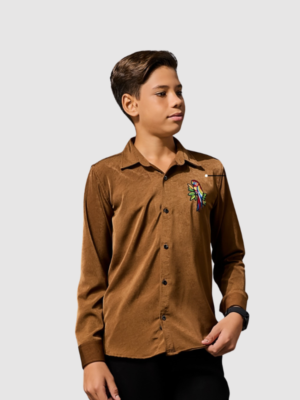 Young boy modeling a long-sleeve, brown shirt with a velvet or suede texture, featuring a small, colorful embroidered parrot detail on the chest.