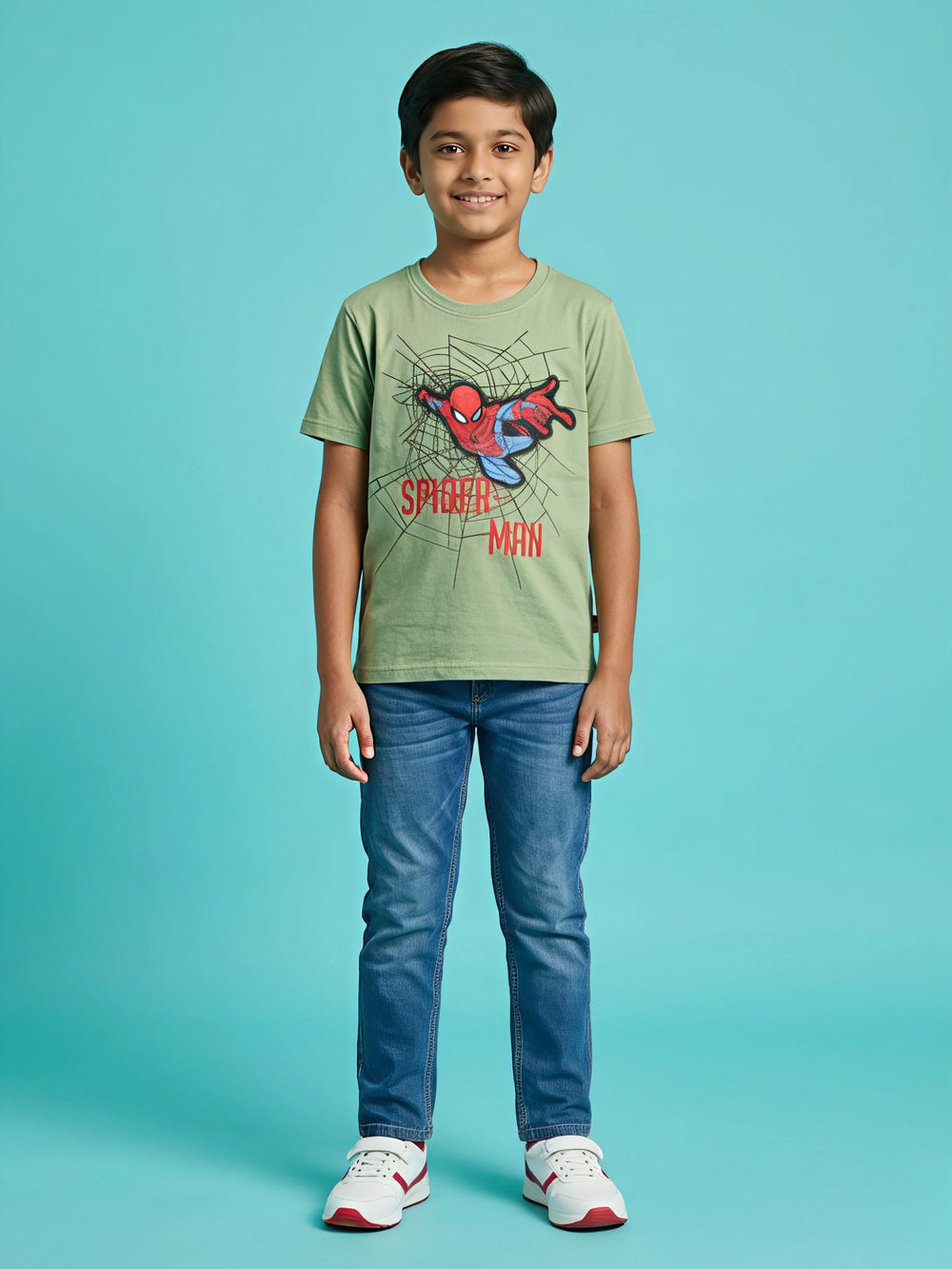 Young boy wearing a comfortable sage green round neck t-shirt featuring a dynamic Spider-Man graphic print with webs and red text, paired with blue jeans and sneakers.