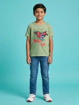Young boy wearing a comfortable sage green round neck t-shirt featuring a dynamic Spider-Man graphic print with webs and red text, paired with blue jeans and sneakers.