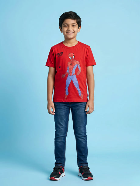 A young boy wearing a bright red short-sleeve crew neck t-shirt with a Spiderman graphic print on the front, paired with blue jeans and sneakers.