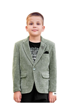 Young boy wearing a sage green corduroy blazer with a lapel pin and black pocket square, styled over a black t-shirt and black trousers.