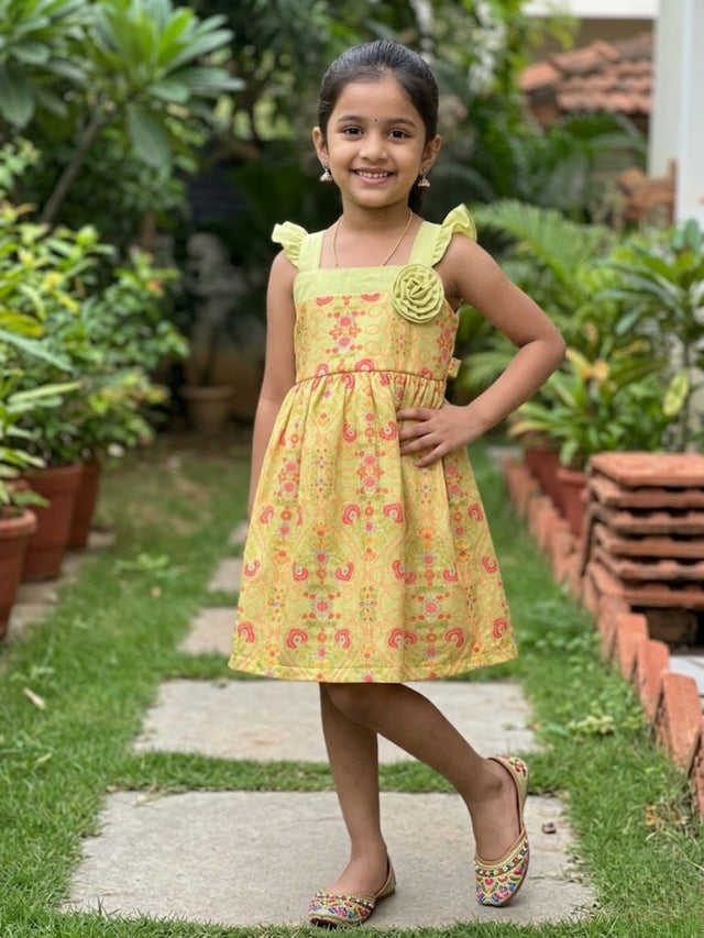 Young girl wearing a lime green floral print frock with ruffle sleeves and a 3D flower accent in a garden setting.