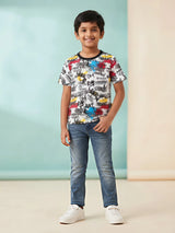 Young boy wearing a white t-shirt with vibrant multicolor graffiti and doodle print, black round neck, short sleeves, and blue jeans.