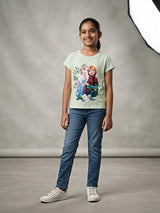 Young girl wearing a light green short-sleeve Disney Frozen graphic t-shirt with Elsa and Anna print paired with blue jeans