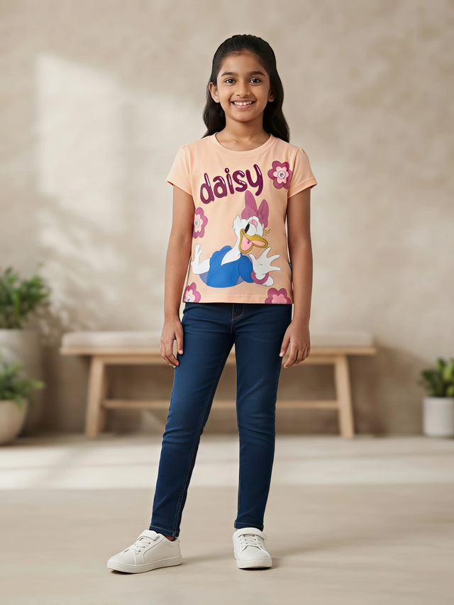 Young girl wearing a peach round-neck graphic top featuring Daisy Duck print paired with dark blue jeans