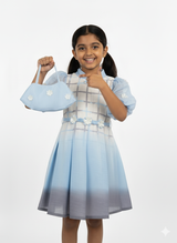 Girls' dress with a gray and white plaid top, a blue ombre pleated skirt, and sheer blue organza puff sleeves with small flower accents.