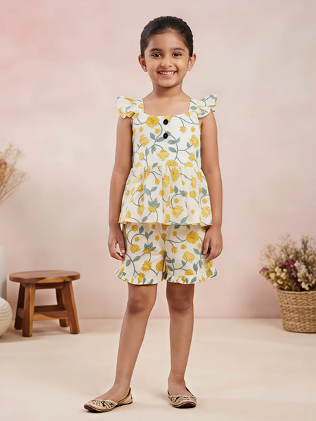 Young girl wearing a cream co-ord set with yellow floral print, ruffle sleeves, and matching shorts.