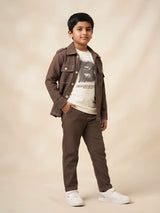 Young boy wearing a brown full sleeve casual shirt with contrast stitching over an off-white graphic t-shirt and matching brown trousers