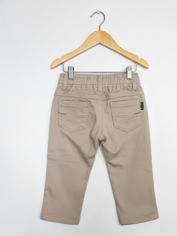 Boys' plain khaki/cream casual pants with an elastic waist, front pockets, and a straight leg fit, hanging on a wooden hanger.