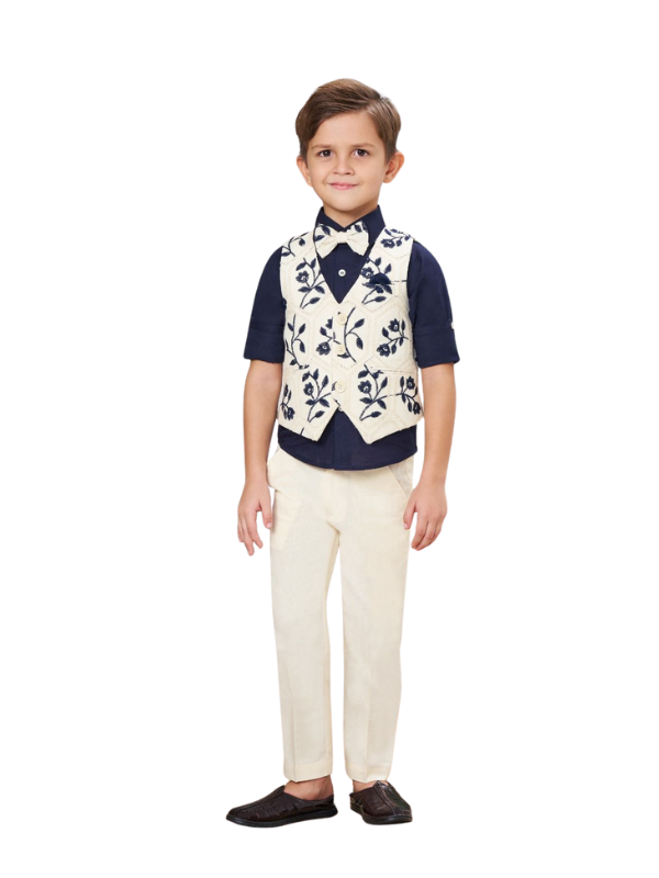 Full-length image of a young boy wearing a three-piece formal set: a cream waistcoat with navy floral embroidery, a navy short-sleeve shirt, a navy bow tie, and cream trousers.