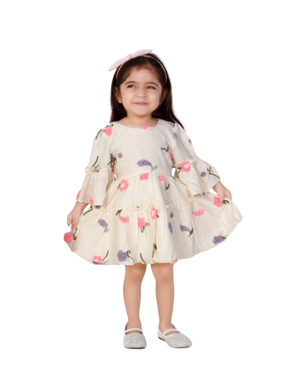 Toddler girl wearing a cream-colored dress with pink and purple floral embroidery, tiered ruffles, and three-quarter bell sleeves.

Export to Sheets