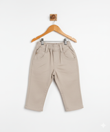 Boys' plain khaki/cream casual pants with an elastic waist, front pockets, and a straight leg fit, hanging on a wooden hanger.