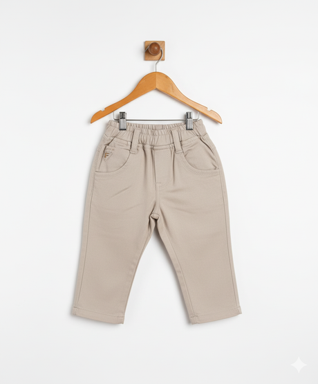 Boys' plain khaki/cream casual pants with an elastic waist, front pockets, and a straight leg fit, hanging on a wooden hanger.
