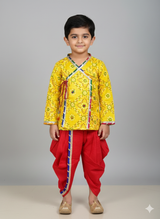 Young boy wearing a long-sleeved yellow printed Angrakha kurta with multi-color trim, paired with traditional red dhoti pants and gold jutis, posing against a grey background.