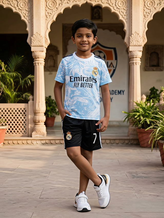 Young boy smiling while wearing a light blue printed sports t-shirt and black athletic shorts coordinate set in a courtyard.