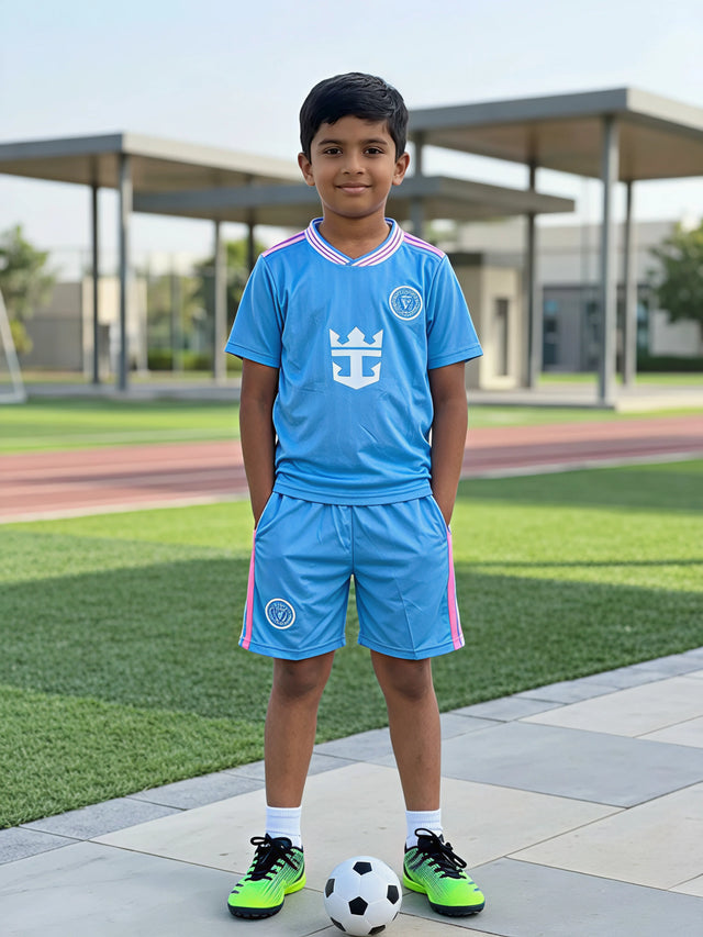 A young boy wearing a blue sports coordinate set with a football on a sports field.