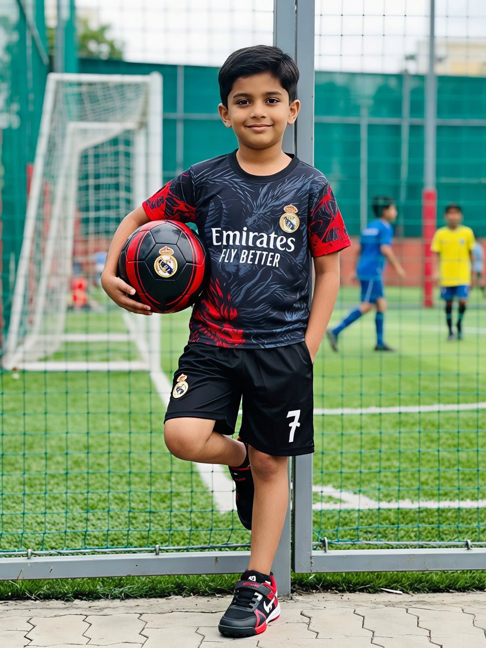A young boy wearing a black football-themed sports coordinate set with graphic prints and the number 7 on the shorts, holding a matching soccer ball on a turf field.