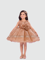 Young girl smiling in a shimmering bronze/brown organza party frock with a full, flared skirt and a large 3D fabric flower on the bodice. The luxurious sleeveless dress is paired with metallic shoes