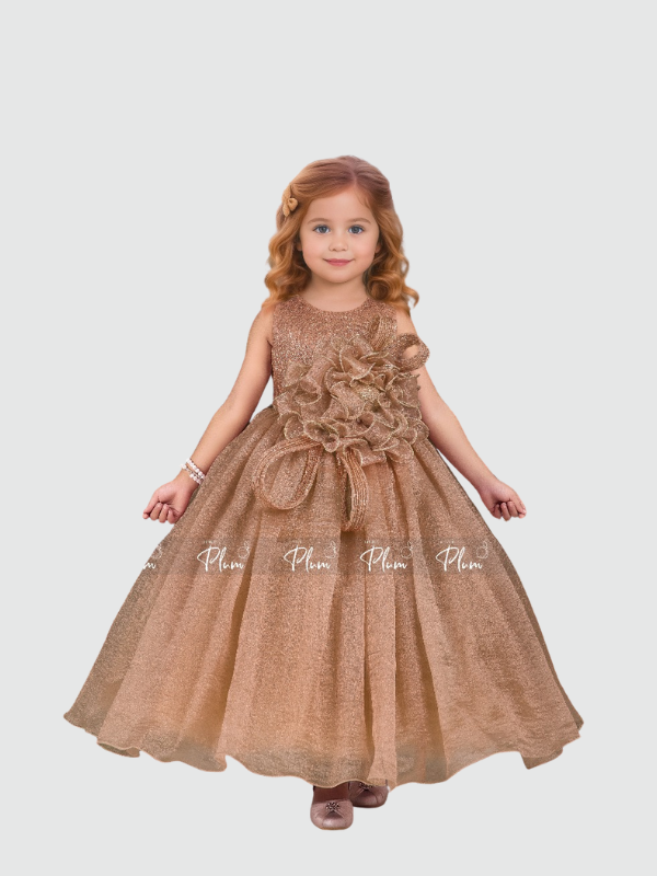 Young girl smiling in a full-length, voluminous rose gold/bronze shimmering party gown. The dress features a large, ruffled 3D flower appliqué on the bodice and a small matching bow at the waist