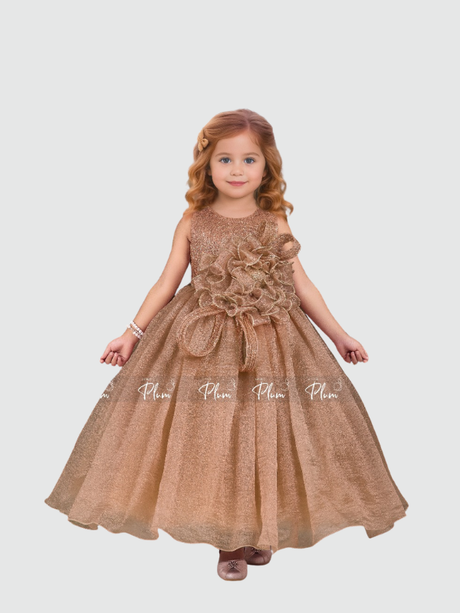 Young girl smiling in a full-length, voluminous rose gold/bronze shimmering party gown. The dress features a large, ruffled 3D flower appliqué on the bodice and a small matching bow at the waist
