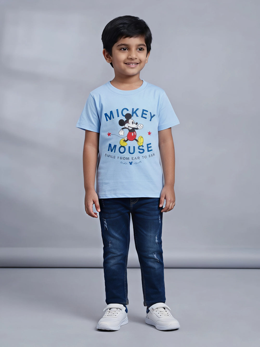 Young boy wearing a light blue Mickey Mouse graphic printed short sleeve crew neck t-shirt paired with dark jeans.