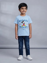 Young boy wearing a light blue Mickey Mouse graphic printed short sleeve crew neck t-shirt paired with dark jeans.