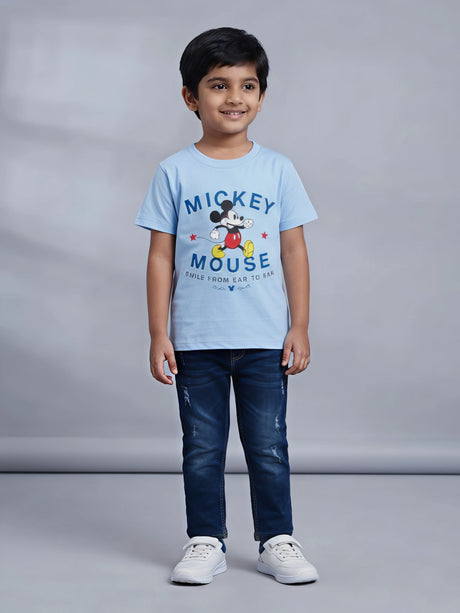 Young boy wearing a light blue Mickey Mouse graphic printed short sleeve crew neck t-shirt paired with dark jeans.