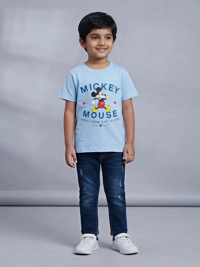 Young boy wearing a light blue Mickey Mouse graphic printed short sleeve crew neck t-shirt paired with dark jeans.