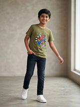Young boy wearing an olive green round neck t-shirt with a Spider-Man superhero graphic print, paired with dark jeans and white sneakers.