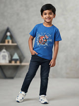 Young boy wearing a blue superhero graphic printed crew neck t-shirt with dark navy jeans and white sneakers
