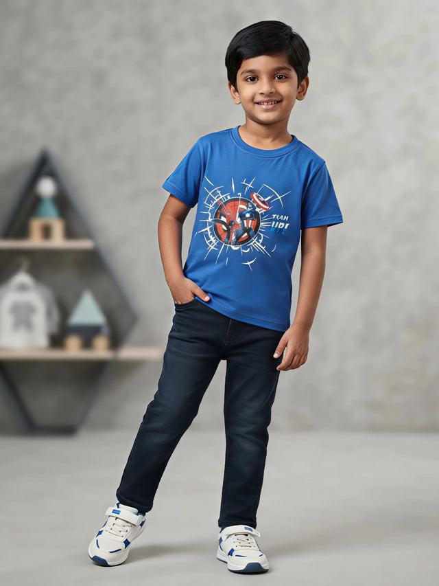 Young boy wearing a blue superhero graphic printed crew neck t-shirt with dark navy jeans and white sneakers