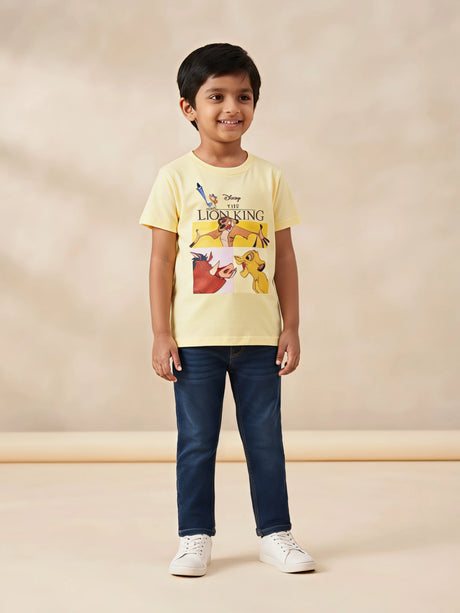 Young boy wearing a light yellow round neck short-sleeve Lion King graphic t-shirt with dark jeans and white sneakers.