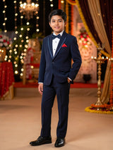 Young boy wearing a navy blue designer coat suit with red pocket square and bow tie for wedding party wear