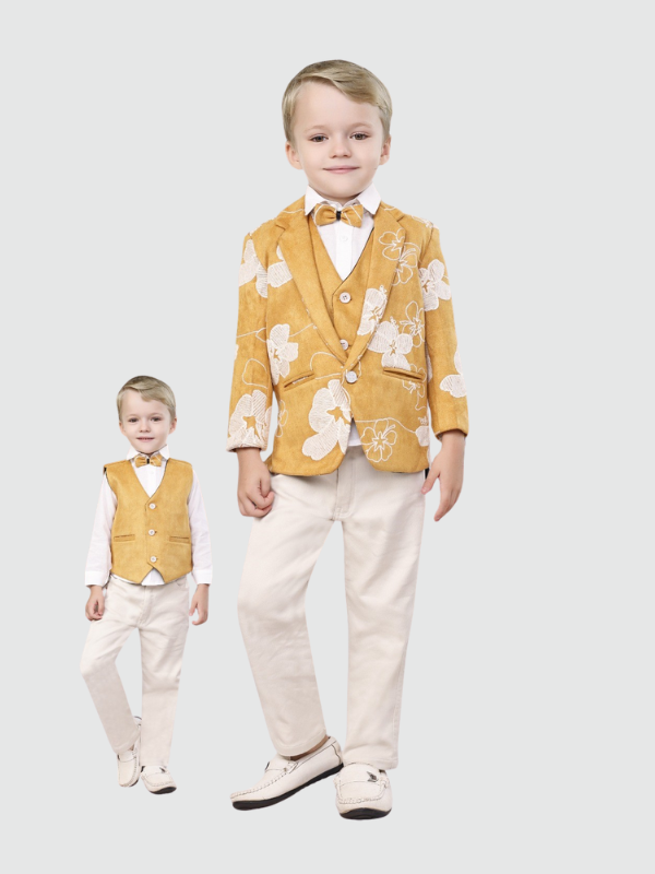 Young boy standing in a bright mustard yellow blazer with white floral print, matching waistcoat, white shirt, and light cream/beige trousers. The set is complete with a yellow bow tie and white loafers