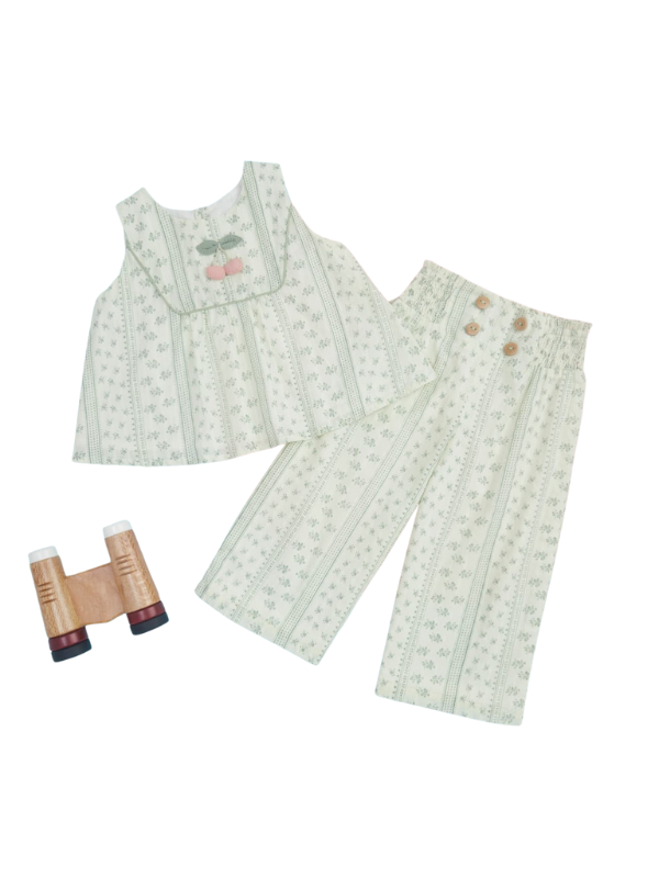 Young girl posing in a fawn/cream colored sharara set featuring a short kurti with floral embroidery and a mirror work neckline, paired with pleated, wide-leg sharara pants and a red dupatta.