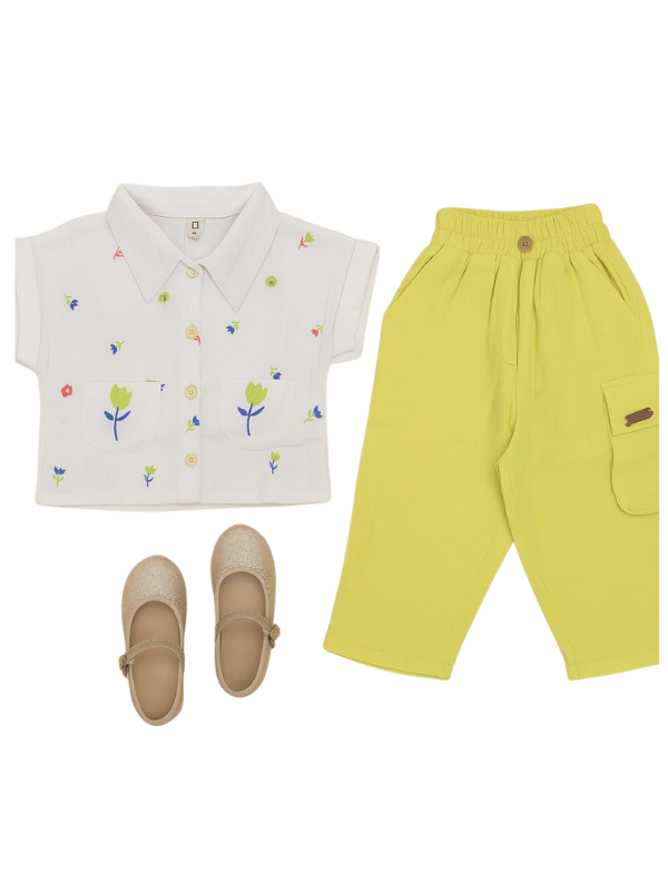 Girls' two-piece set featuring a white short-sleeve collared shirt with colorful floral embroidery, paired with bright neon lime green cargo pants with an elastic waist, and gold glitter Mary Jane shoes.