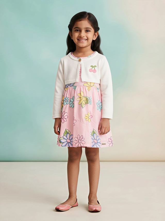 Young girl wearing a peach floral printed frock paired with a full-sleeve white koti jacket featuring a cherry accent.