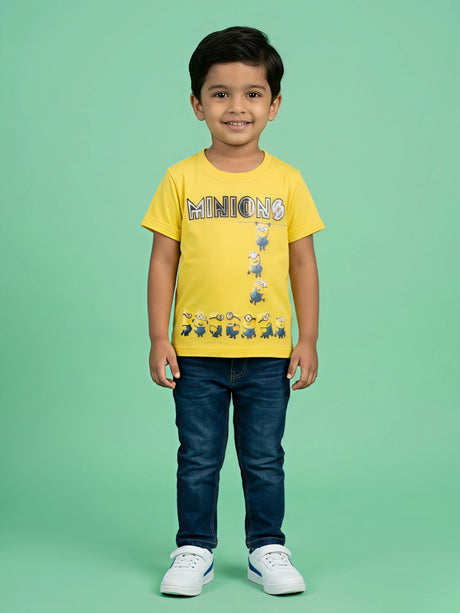 A young boy wearing a bright yellow short-sleeve crew neck t-shirt with a Minions graphic print on the front, paired with dark blue jeans and white sneakers.