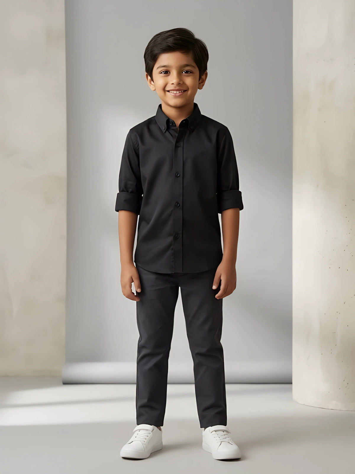 Young boy wearing a stylish solid black casual shirt with folded sleeves and matching dark trousers