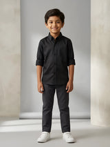 Young boy wearing a stylish solid black casual shirt with folded sleeves and matching dark trousers